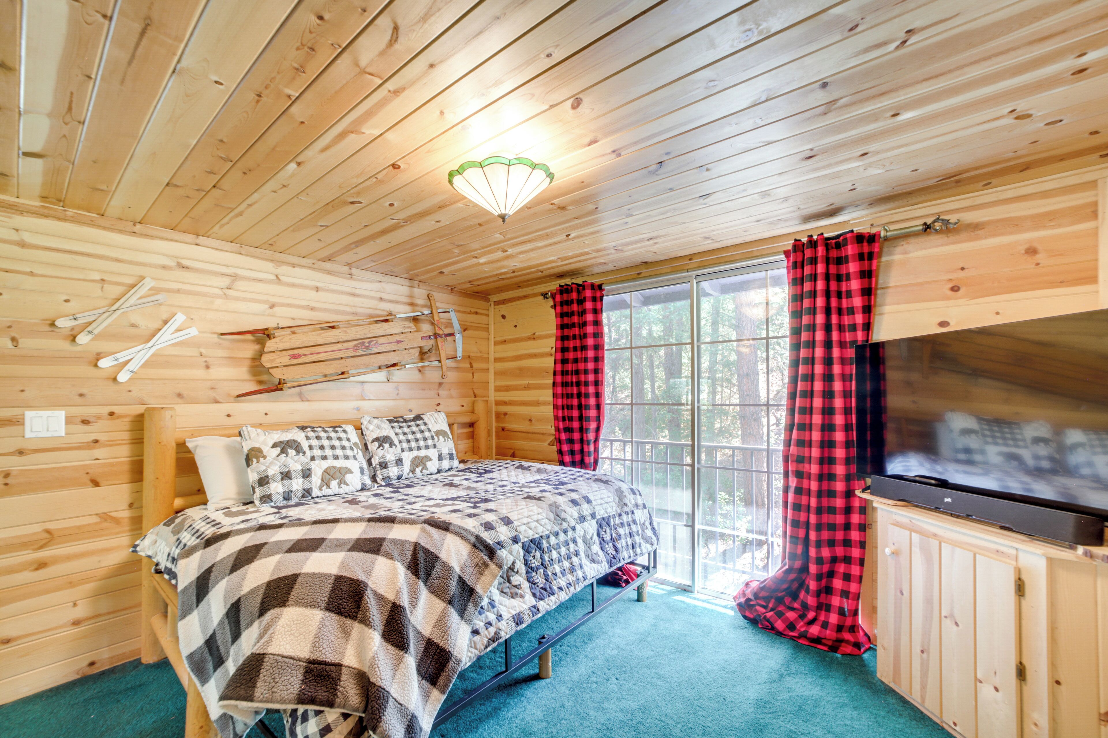 Camera da letto in una baita di legno, con un letto, una televisione e un'ampia finestra con tende.