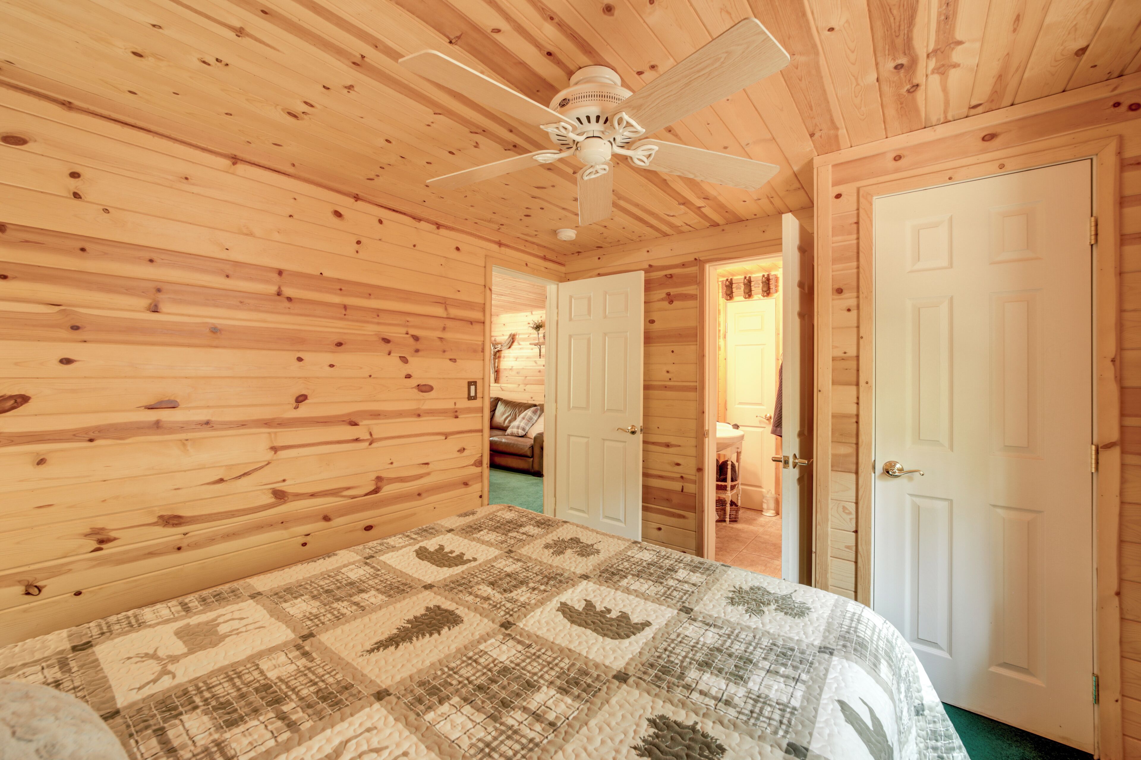 A wooden cabin bedroom with a ceiling fan, a bed with a patterned quilt, and two white doors.