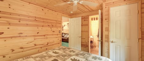A wooden cabin bedroom with a ceiling fan, a bed with a patterned quilt, and two white doors.