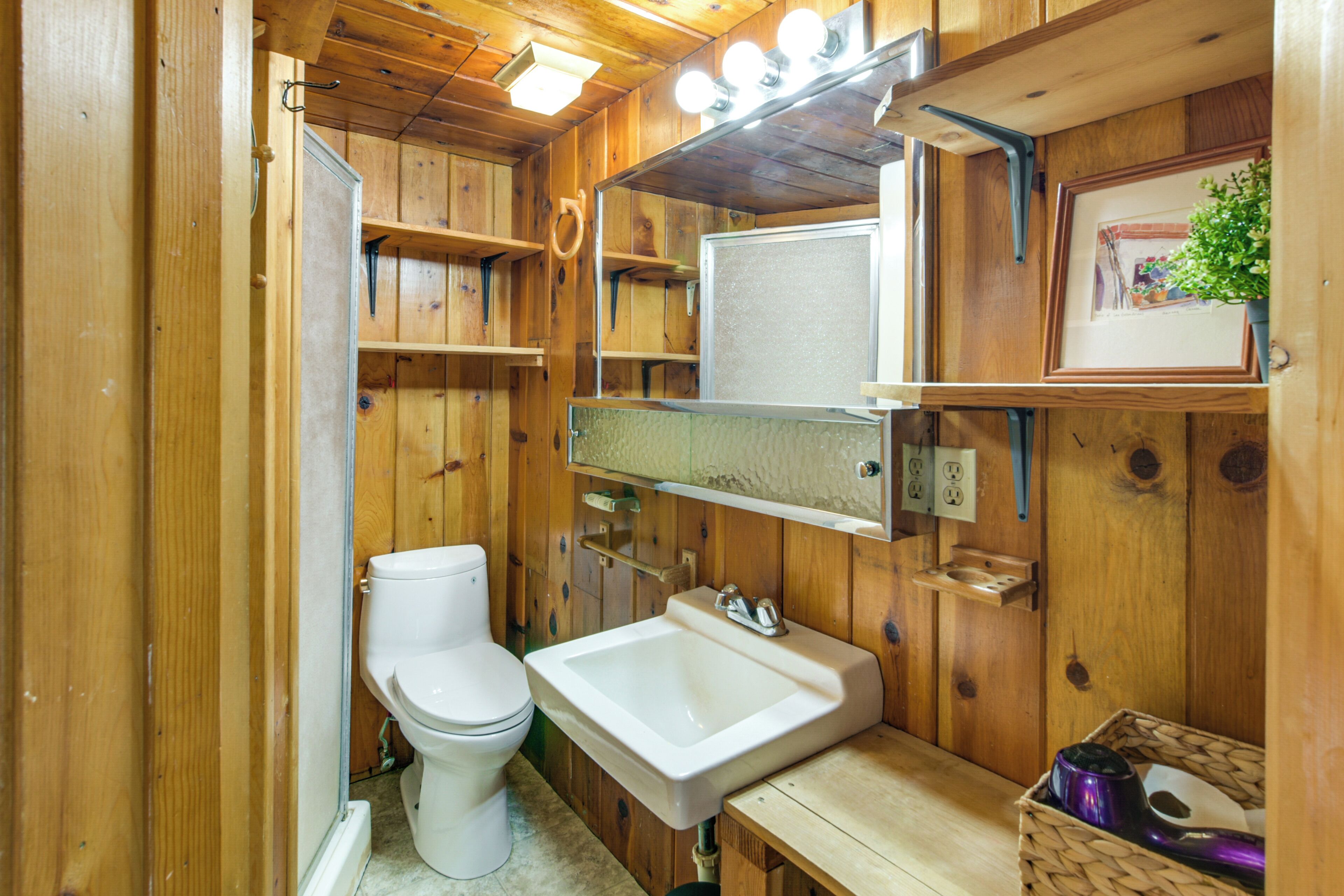 Une salle de bain en bois avec des toilettes, un lavabo et des étagères.