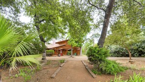 A rustic cabin with a dirt path leading to the entrance, surrounded by lush greenery and tall trees.