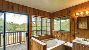 A wooden cabin bathroom with a large bathtub, a sink, and a mirror.