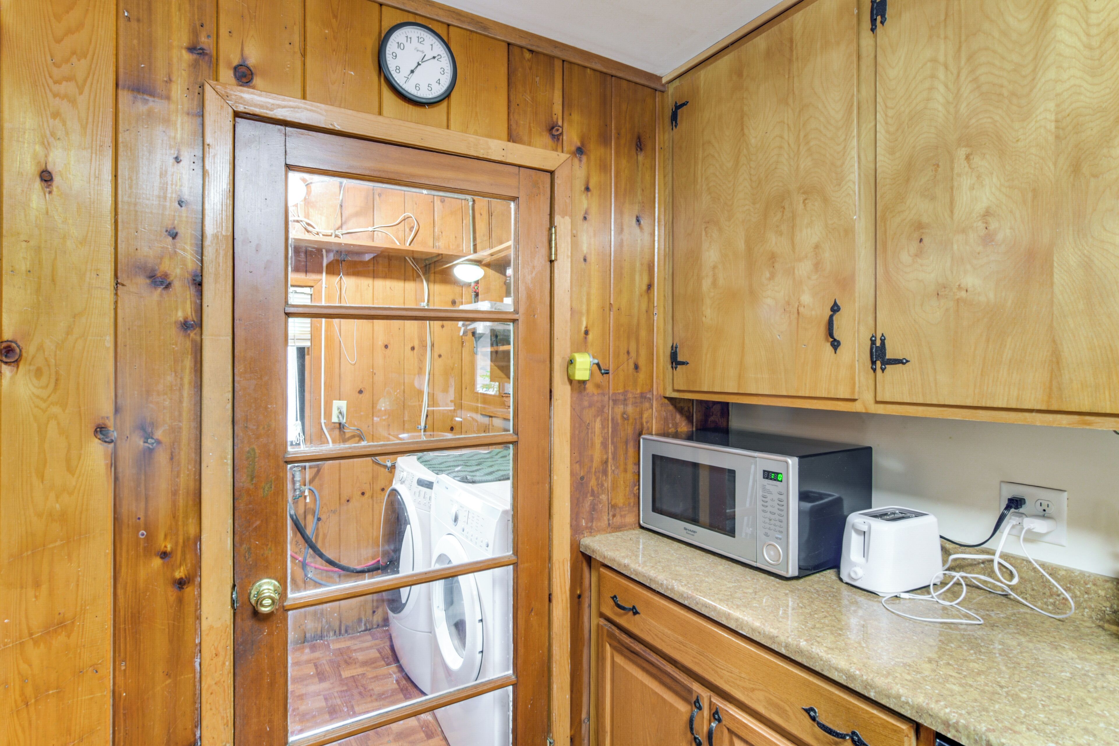 A kitchen with wooden cabinets, a microwave, a toaster, and a washing machine visible through a glass door.