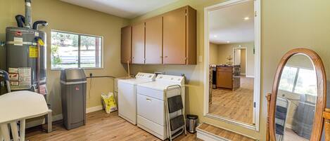 A laundry room with a washer and dryer, a vacuum cleaner, a mirror, and a window with a view of the outdoors.