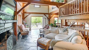 A spacious living area with a stone fireplace, wooden beams, and a balcony with wooden railings. - Riverfront Hudson Valley Gem w/ Beach Access! (Athens)