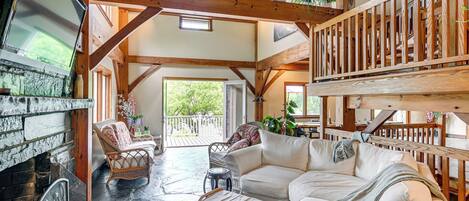 Un vaste espace de vie agrémenté d’une cheminée en pierre, de poutres apparentes et d’un balcon doté de balustrades en bois.