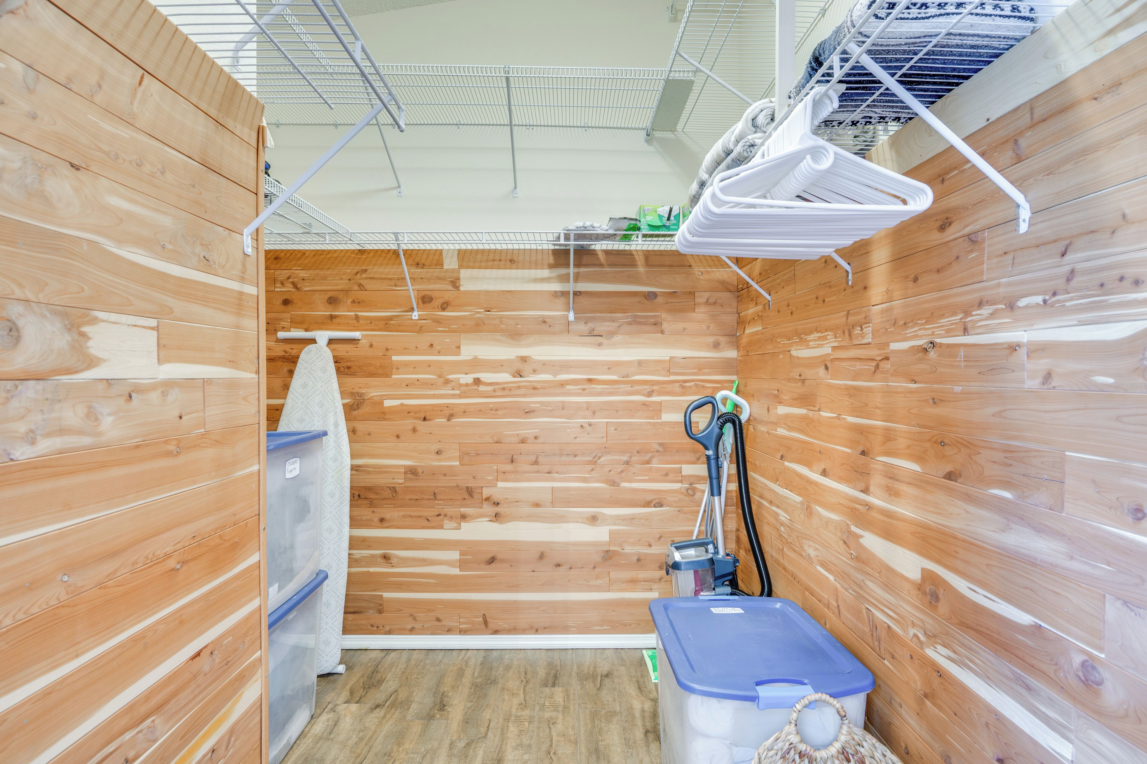 Une petite pièce aux murs lambrissés, équipée d’une douche, d’un porte-serviettes, d’un aspirateur et d’un bac de rangement.