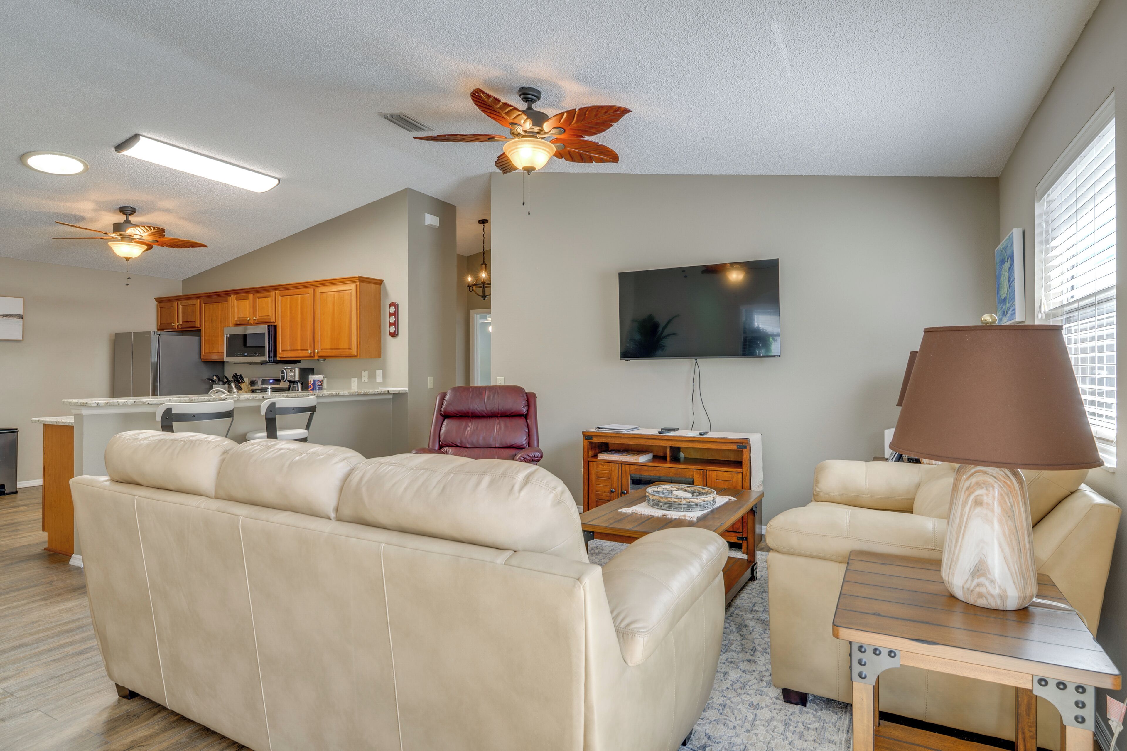 A modern living room with a beige sofa, a wooden coffee table, a red chair, and a ceiling fan.