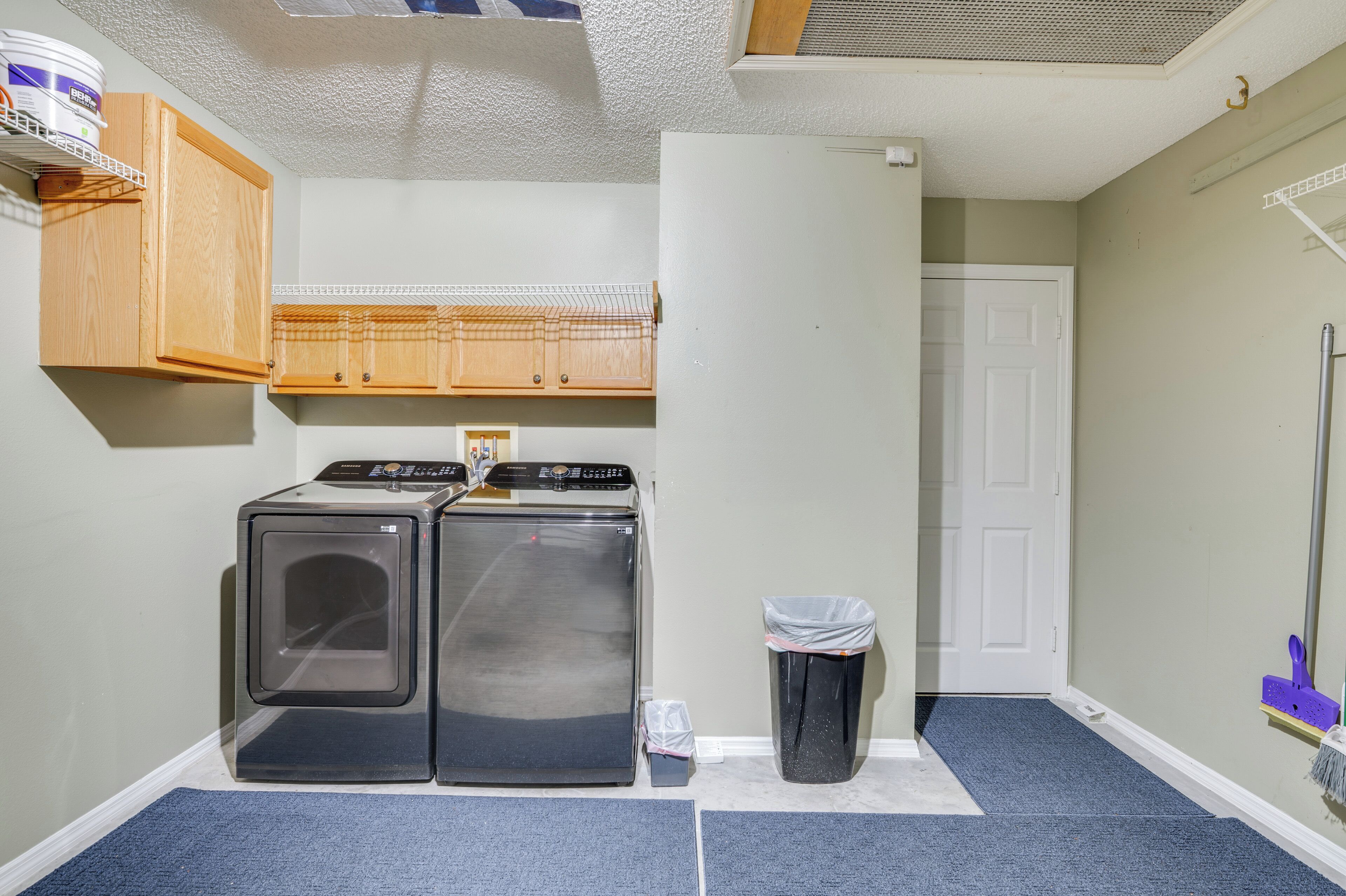 A laundry room with two stacked washers and dryers, a trash can, and a door leading to another room.