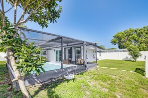 Ein modernes Haus mit überdachter Terrasse, Schwimmbad und gepflegtem Rasen.