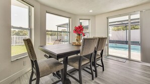 Un comedor con mesa y sillas, ventanas amplias y vista a una piscina.