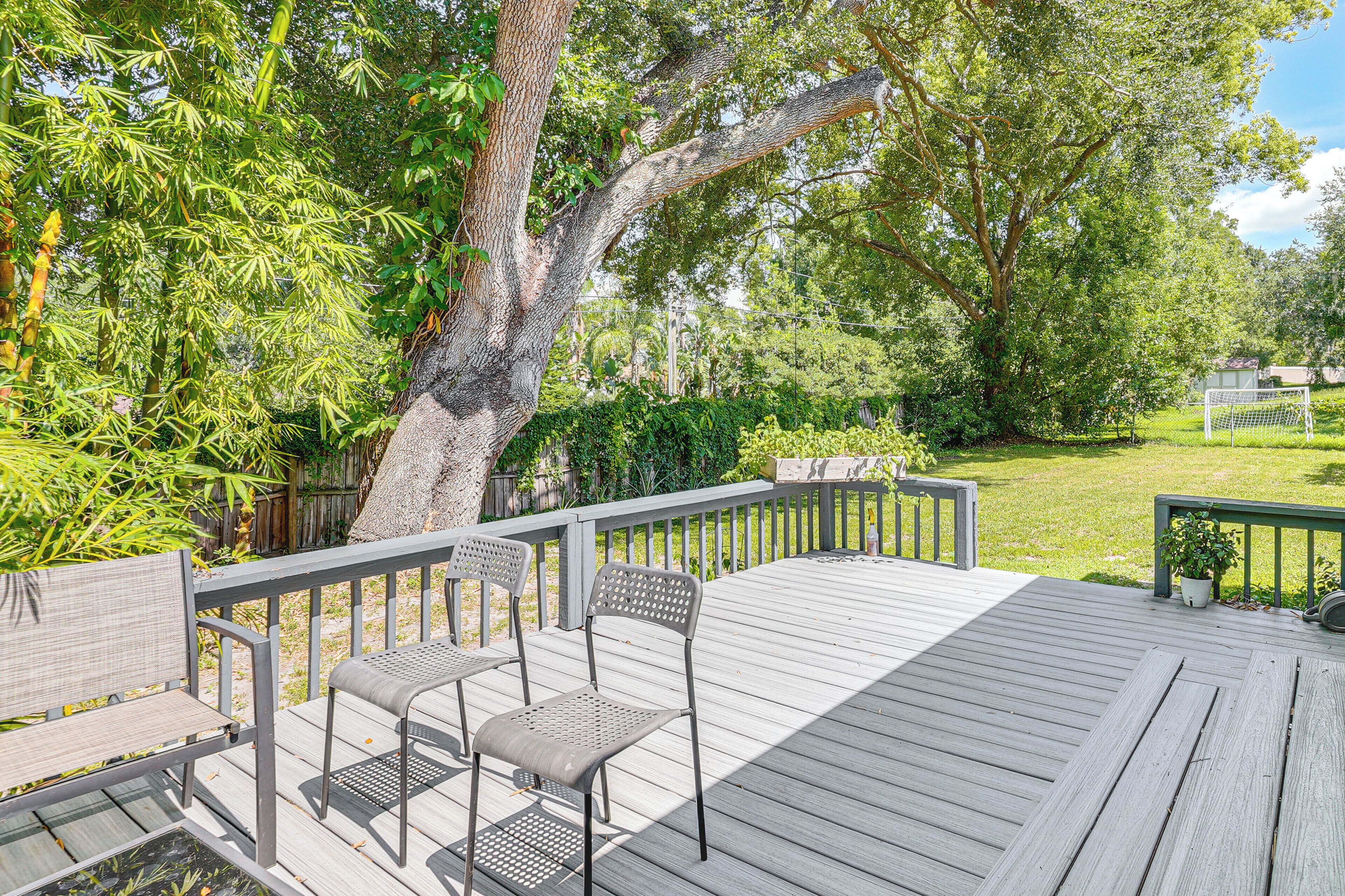 A wooden deck with chairs and a table, surrounded by lush greenery and trees.