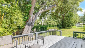 A wooden deck with chairs and a table, surrounded by lush greenery and trees. - Group Getaway w/ Deck & Yard in Lakeland! (Lakeland)