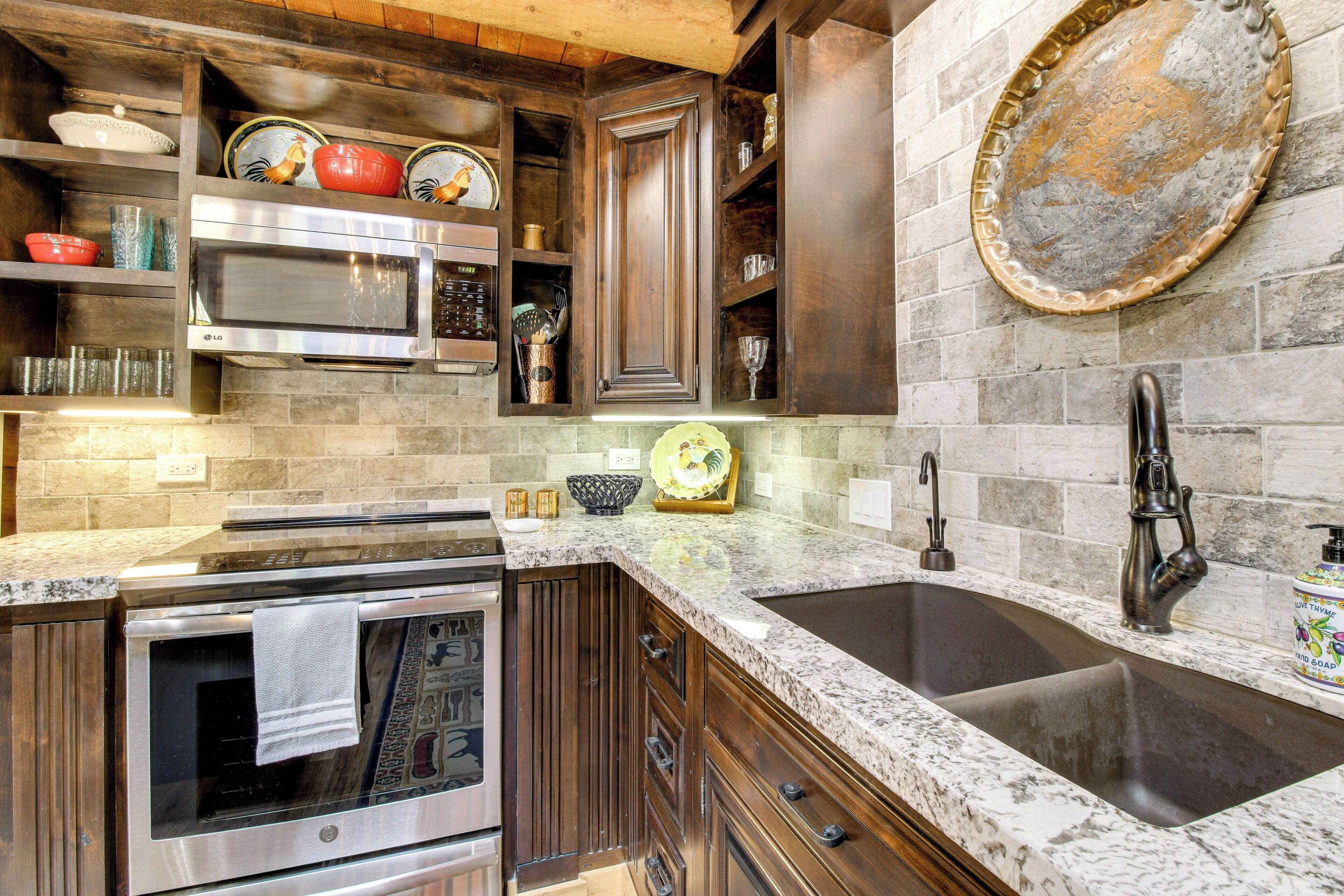A kitchen with granite countertops, stainless steel appliances, wooden cabinets, and a stone backsplash.