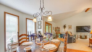 A dining area with a wooden table set for four, surrounded by chairs. There is a chandelier above the table, and a television is visible in the background. - 3 Mi to Dtwn Jefferson City: Family Home w/ Deck (Jefferson City)