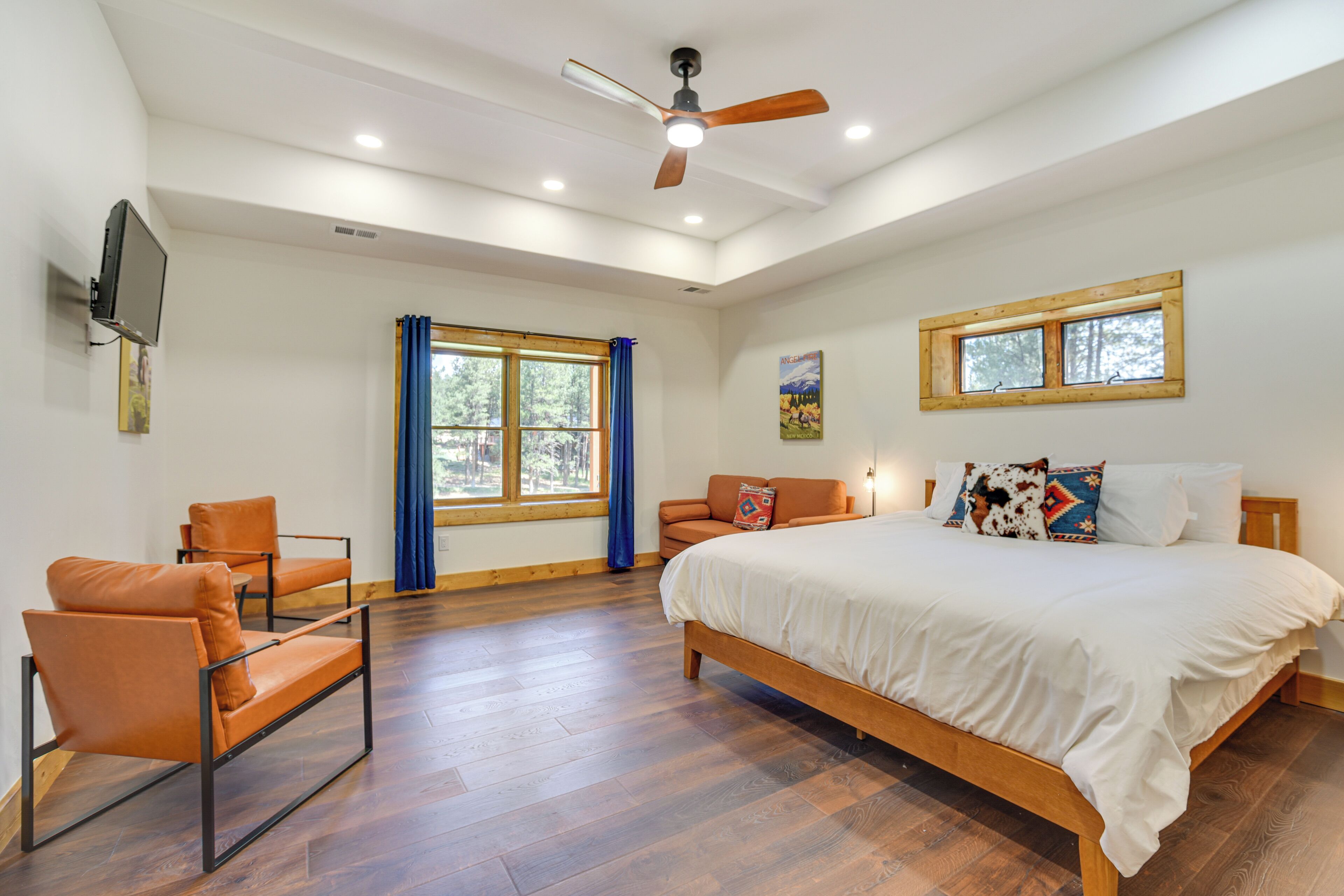 A bedroom with a large bed, two chairs, a ceiling fan, a TV, and a window with curtains.