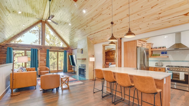 A spacious kitchen with wooden cabinets, a large island with bar stools, and a view of the outdoors through large windows. - 3 Mi to Resort: Year-round Angel Fire Getaway! (Angel Fire)