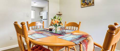 A dining area with a wooden table and chairs, a vase with flowers, and a painting on the wall.