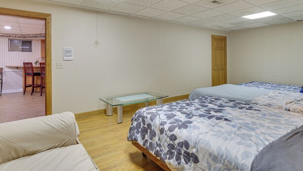 Un dormitorio con dos camas, una mesita de vidrio, una puerta de madera y una kitchenette al fondo.