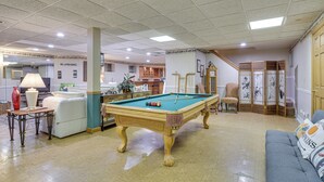 Una mesa de billar en una habitación con un sofá, una lámpara y una silla.