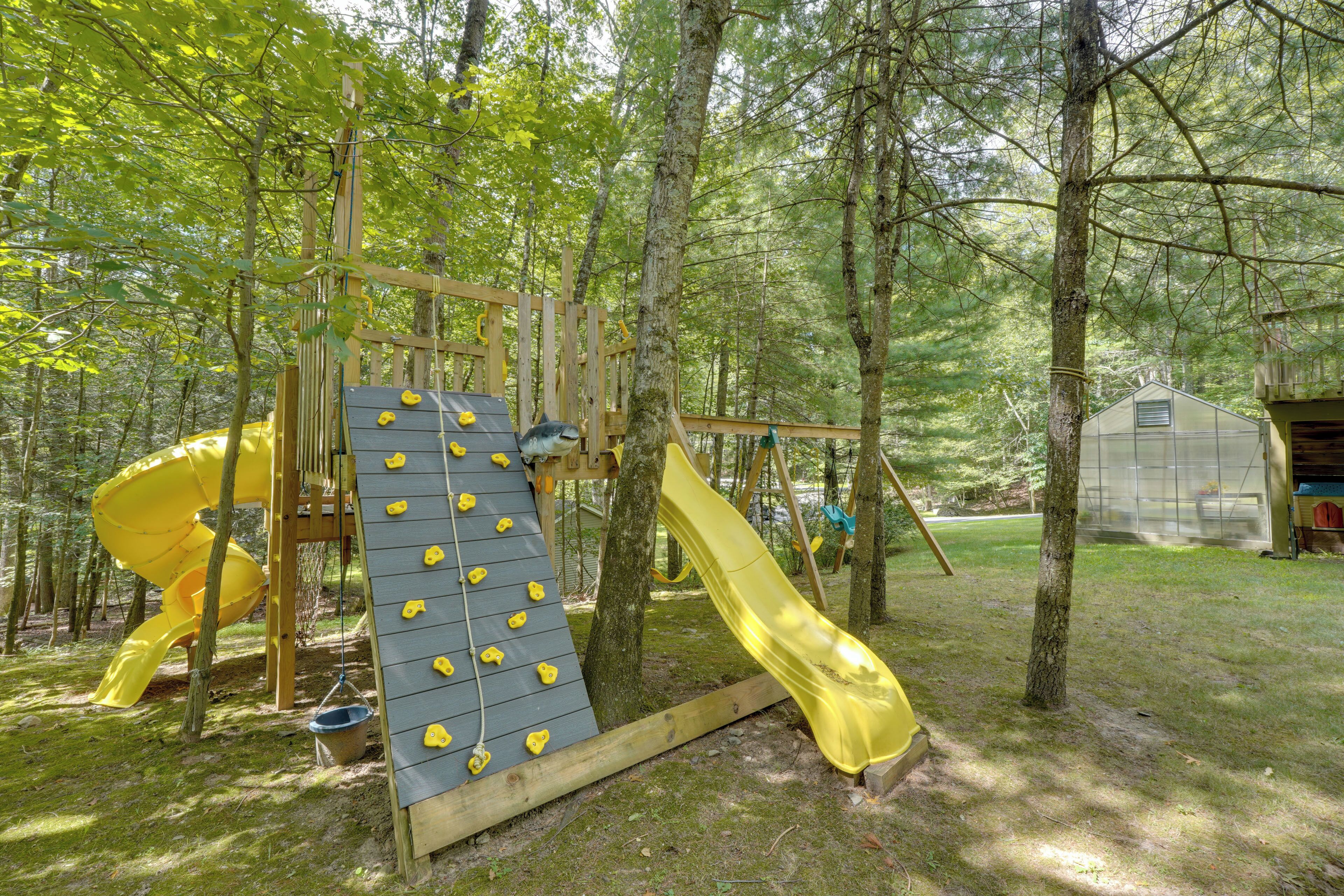 A playground with a slide and climbing wall in a wooded area.