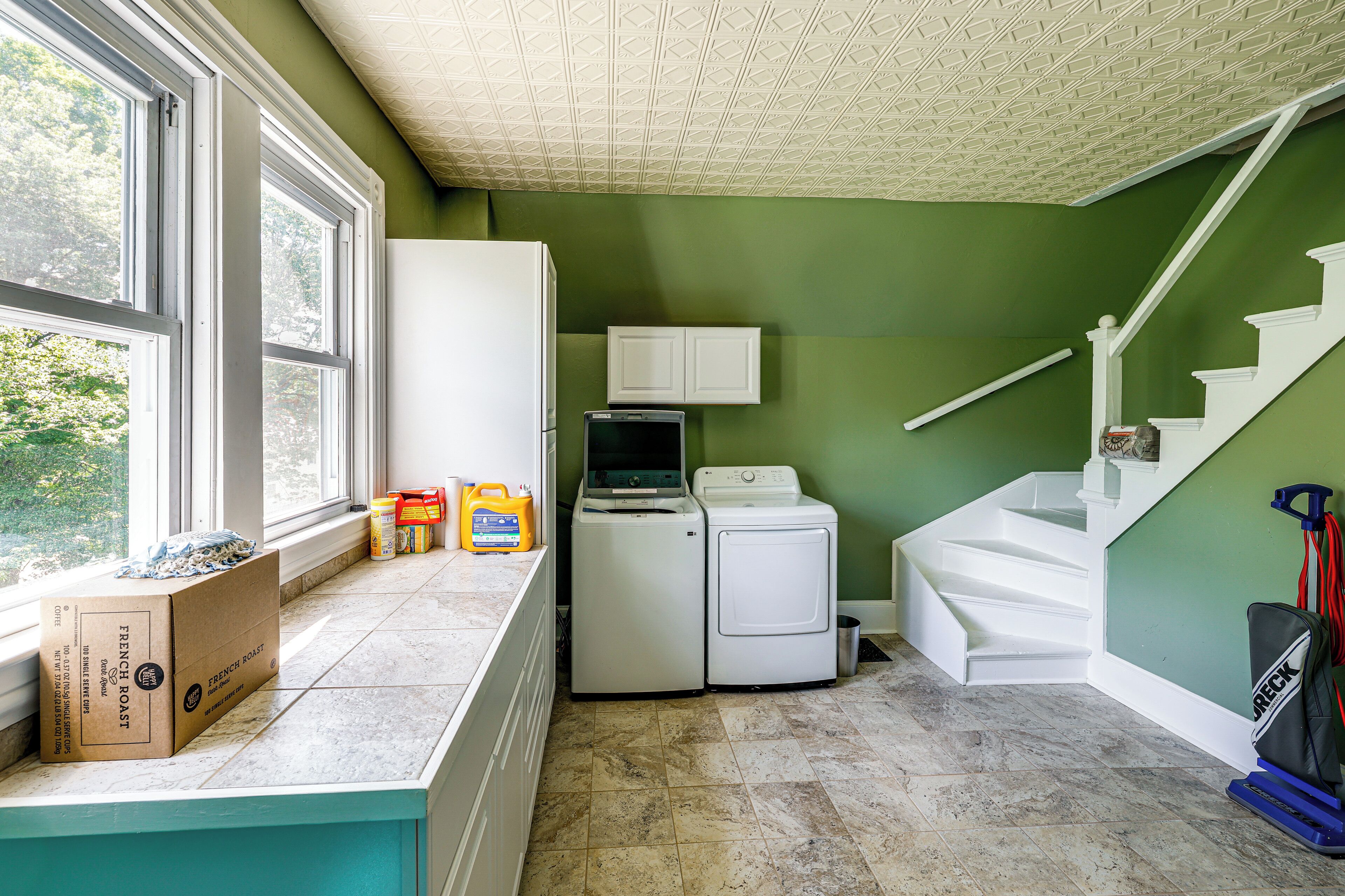 Une buanderie équipée d’un lave-linge et d’un sèche-linge, avec une fenêtre, un meuble et une boîte posée sur le comptoir.