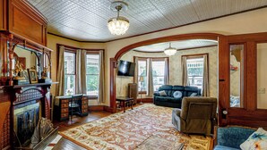 A spacious living room with a fireplace, a large rug, a sofa, and a television. - 2-acre Property: Victorian Home in Brownville! (Brownville)