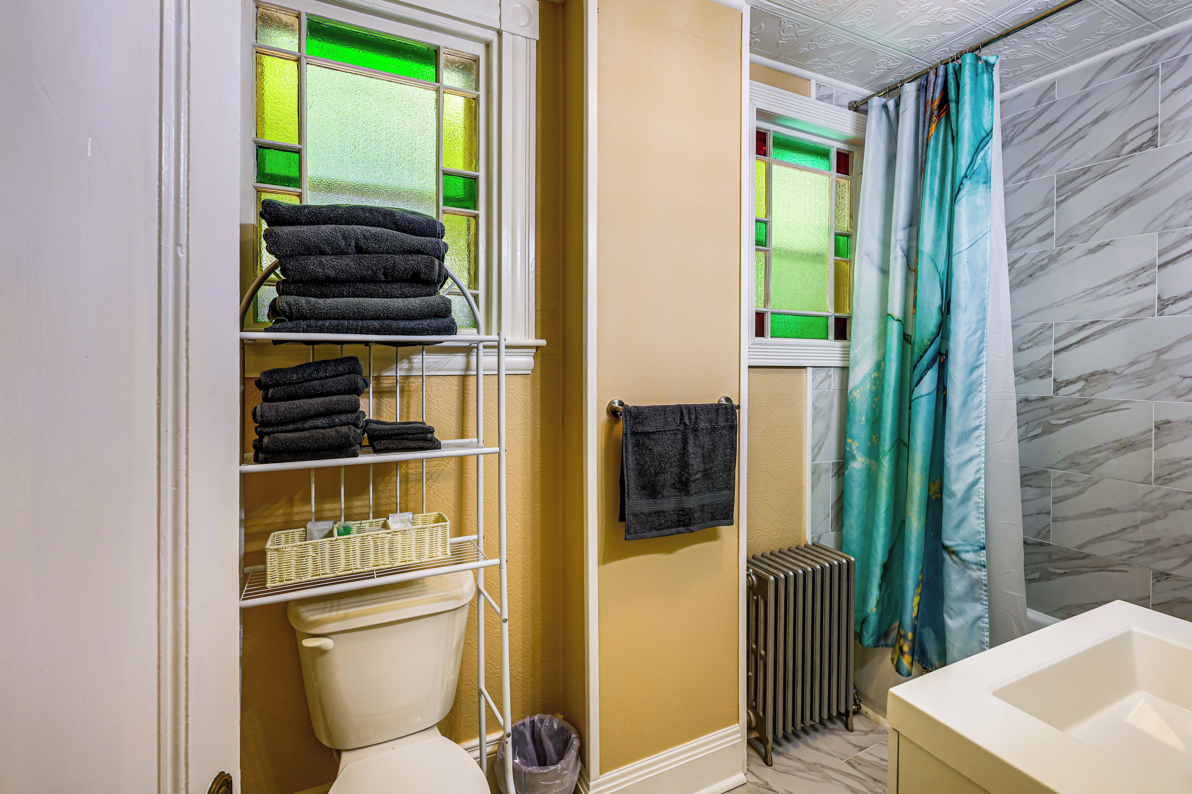 A bathroom with a toilet, a shelf with towels, a radiator, and a shower curtain.
