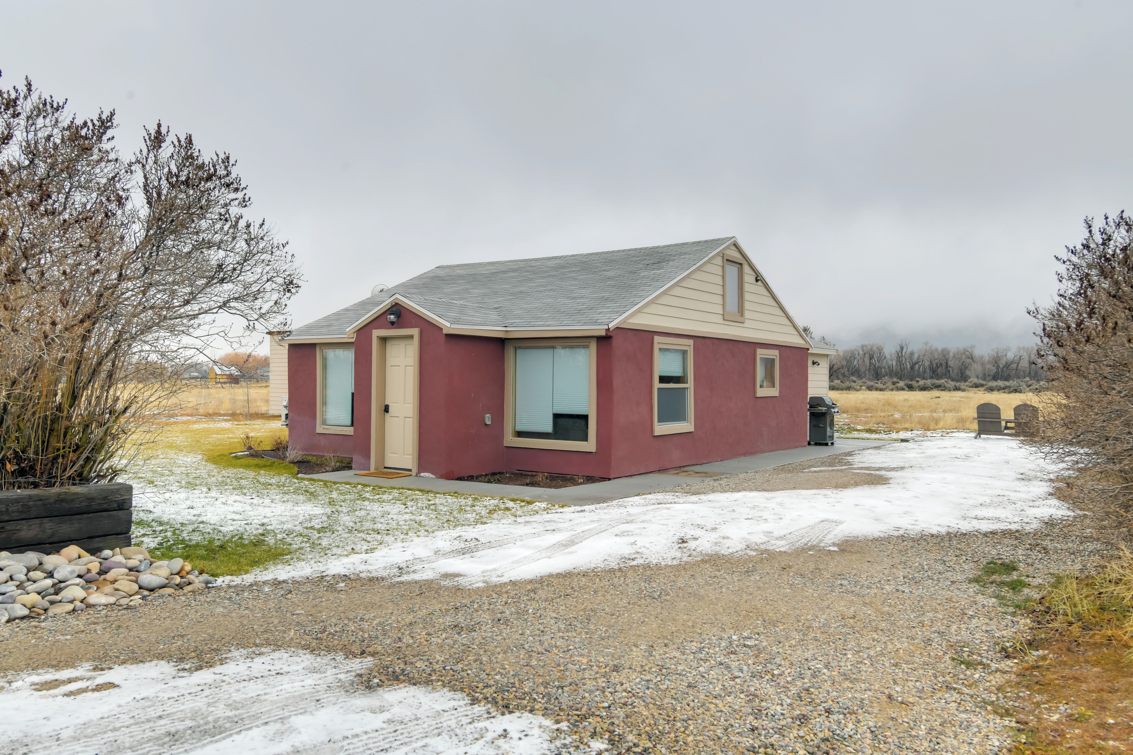 A small, single-story building with a red exterior and beige trim, located in a rural area with a gravel driveway and sparse vegetation.