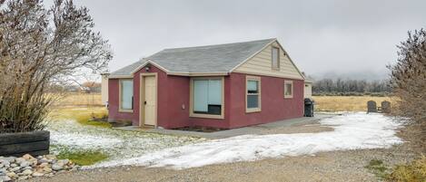 A small, single-story building with a red exterior and beige trim, located in a rural area with a gravel driveway and sparse vegetation.