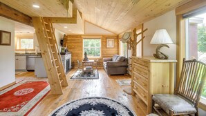 Interior acollidor d'una cabana amb terres de fusta, una llar de foc, un sofà, una taula de dinar i una escala.