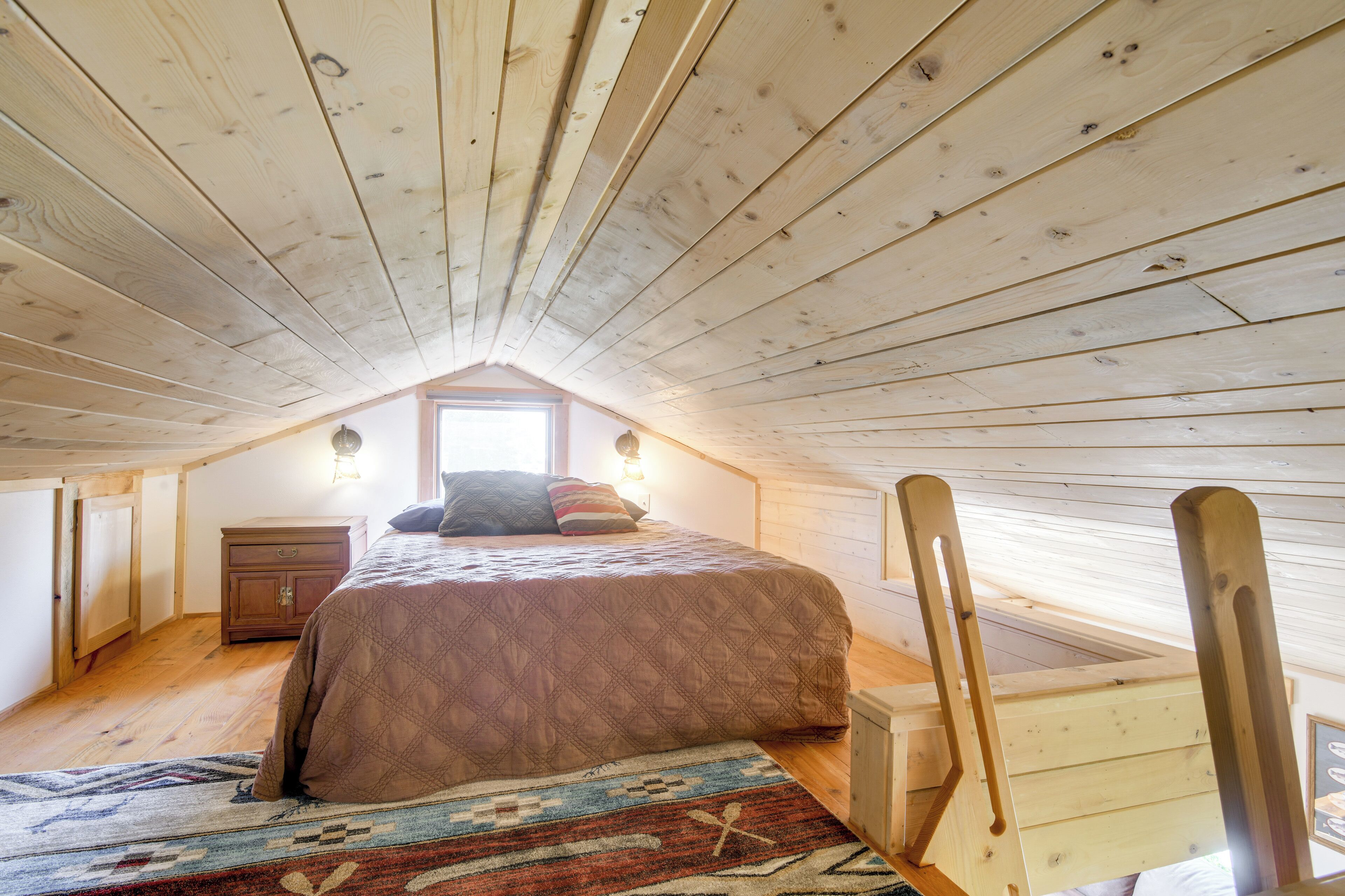 Un dormitorio con techo de madera, una cama con colcha, una mesita de noche y una ventana.
