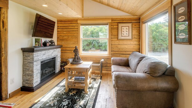 Una habitació acollidora amb una llar de pedra, parets de fusta, una finestra gran i un sofà confortable.
