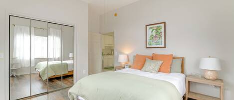 A bedroom with a large bed, a bedside table with a lamp, a mirror, and a painting on the wall.