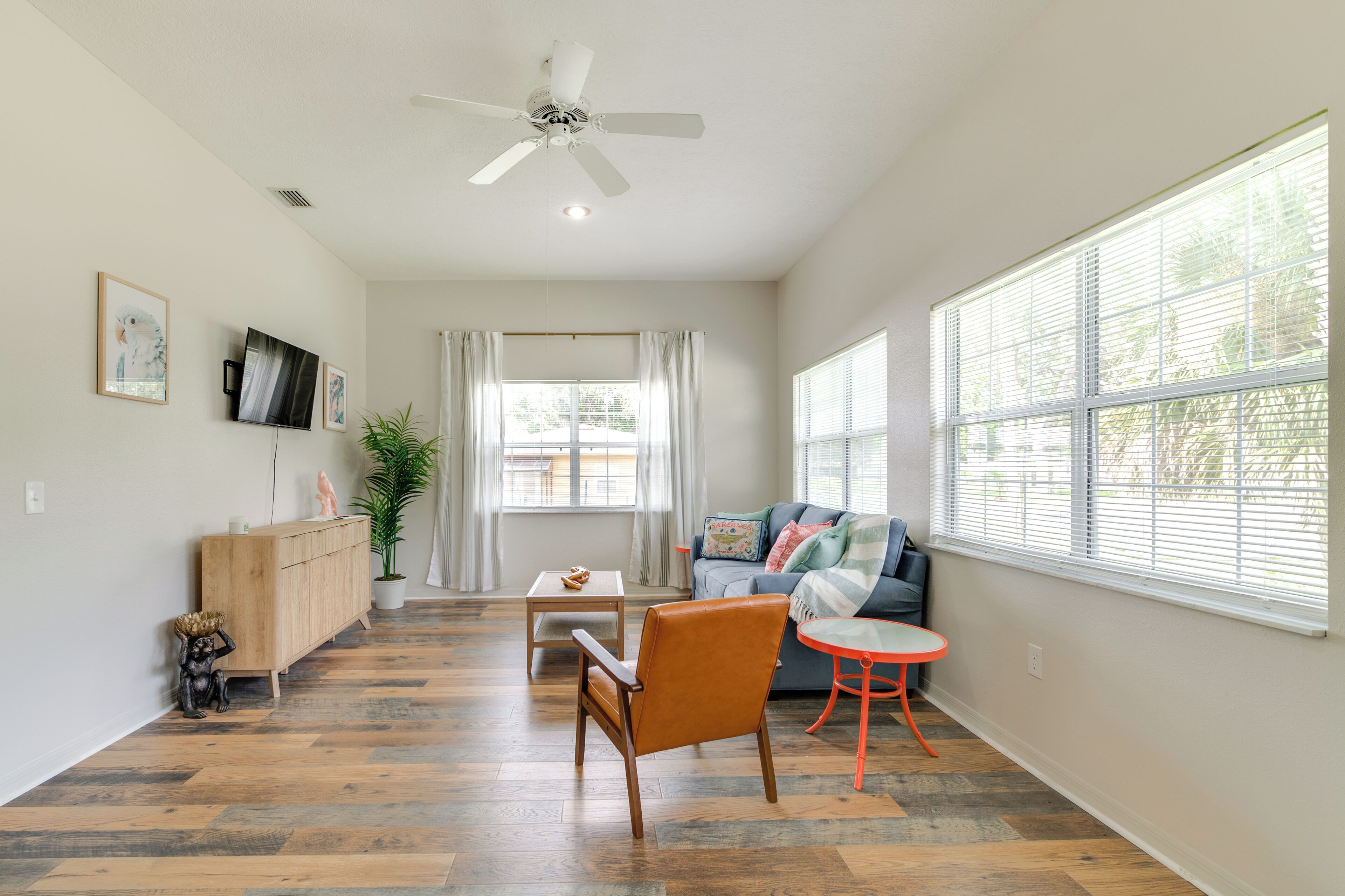 A spacious living room with a wooden floor, a ceiling fan, a sofa, a coffee table, and a small orange table.