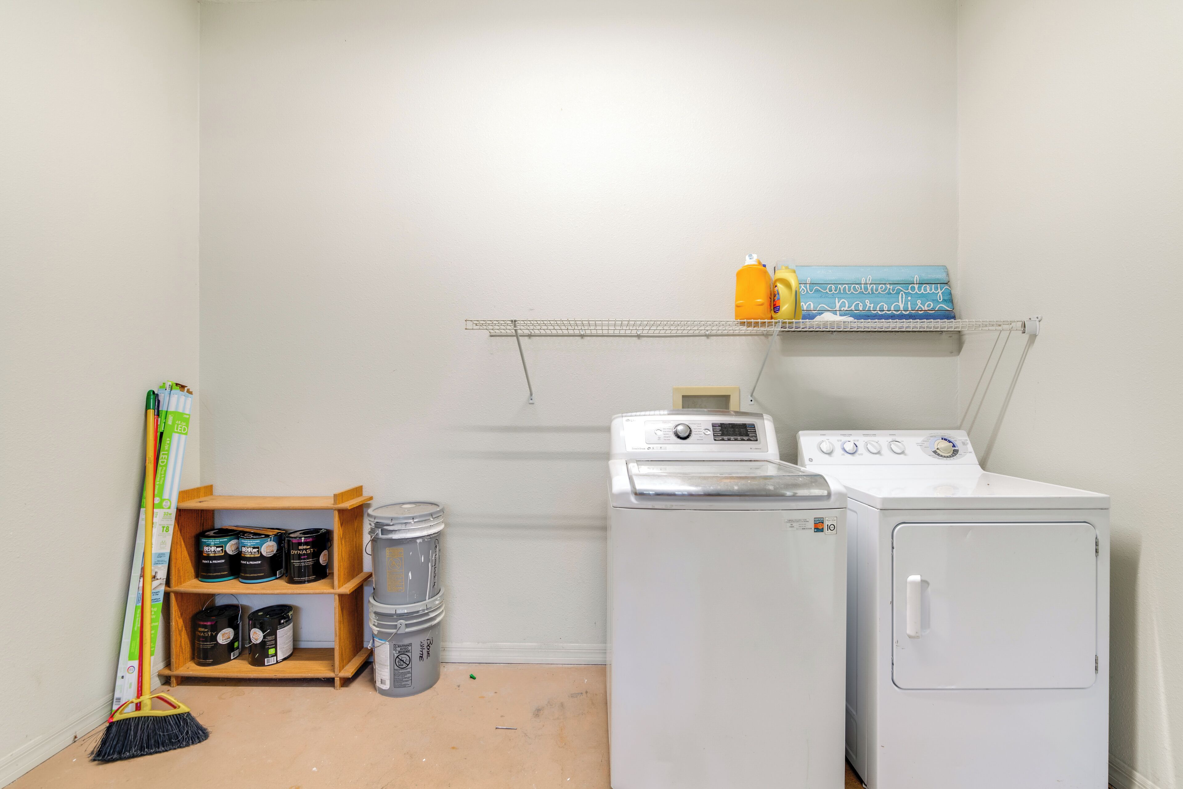 A laundry room with a washing machine, dryer, shelves with cleaning supplies, and a broom.