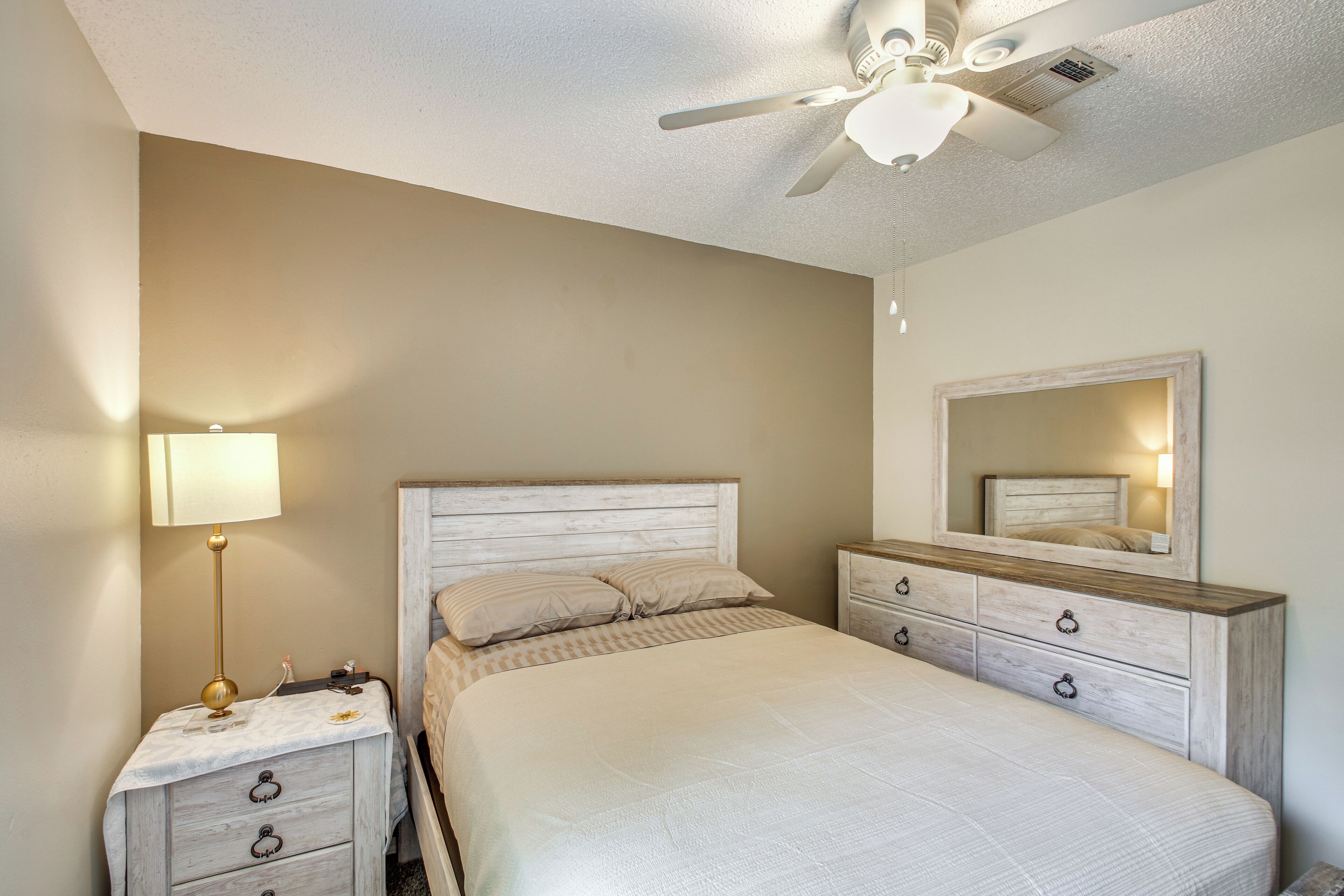 A bedroom with a bed, nightstand, dresser, mirror, ceiling fan, and lamp.
