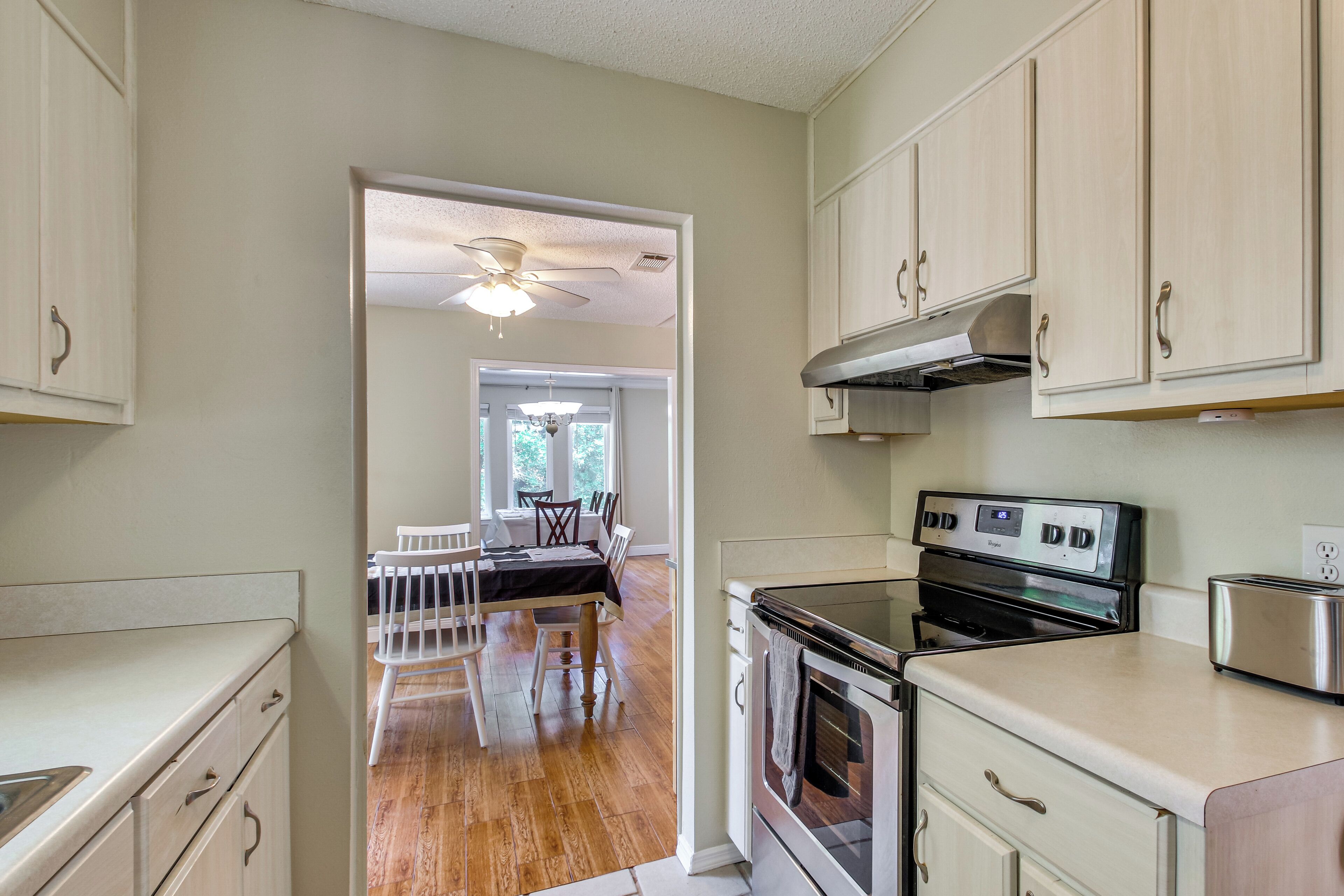 A kitchen with white cabinets, a stove, and a toaster. There is a dining area with a table and chairs visible through an open doorway.