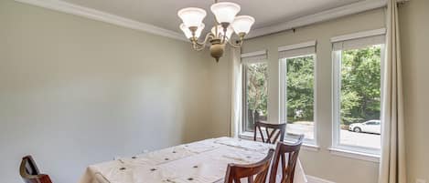 Comedor con una mesa dispuesta para cuatro, una araña y ventanas amplias con cortinas.