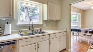 A kitchen with a window, sink, and cabinets. There is a dining area with a table and chairs visible through the window. - Shop, Dine & Visit Uwf: Pensacola Home w/ Yard! (Pensacola)