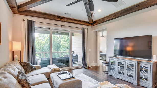 A spacious living room with a large sectional sofa, a flat-screen TV, and a sliding glass door leading to an outdoor patio. - Community Perks: Mountain-view Condo in Toccoa! (Toccoa)