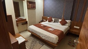 A bedroom with a bed, bedside tables, a mirror, a wall-mounted artwork, and a patterned wall panel. - Hotel Red Rose  (Vadodara)