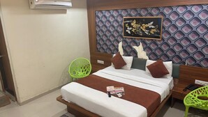 A hotel room with a bed, a wooden headboard, a wall-mounted air conditioner, a green chair, and a patterned wall. - Hotel Red Rose  (Vadodara)