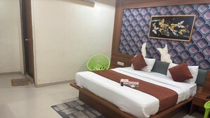 A neatly made bed with a brown headboard, a green chair, and a patterned wall. - Hotel Red Rose  (Vadodara)