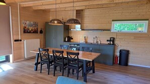 A wooden interior with a dining table, chairs, a kitchen area, and a window.