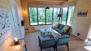 A spacious room with a large window, a sofa, a coffee table, and a wall-mounted TV.
