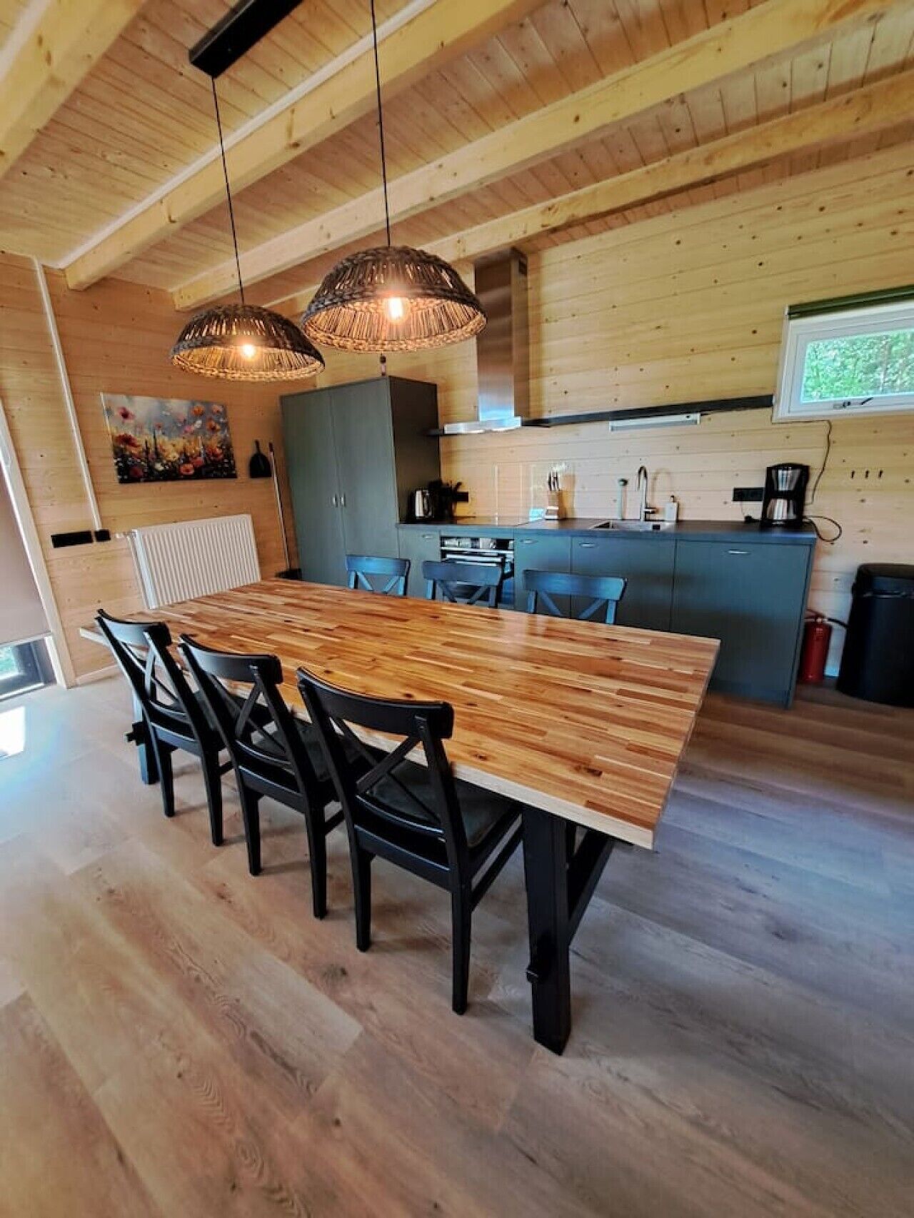 A wooden dining table with chairs, a kitchen area with a stove, and a hanging light fixture.