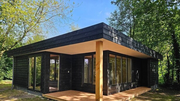 A modern house with large windows, a wooden deck, and a natural surrounding.