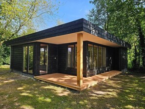 A modern house with large windows, a wooden deck, and a natural surrounding.