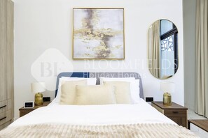A bedroom with a large bed, two bedside tables, a mirror, and a wall-mounted artwork.